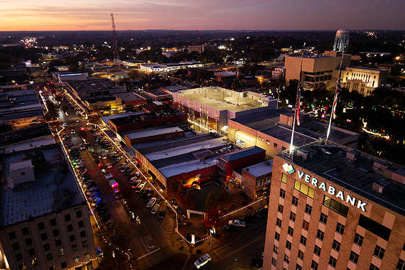 An aerial view of downtown Longview, Texas at dusk, with holiday lights outlining the rooftops of Main Street buildings and the VeraBank tower lit in the foreground.